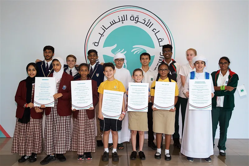 Students holding multilingual tolerance pledges in front of the Human Fraternity Meeting logo